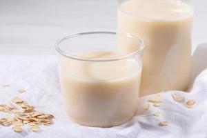 copo de close-up de leite de aveia e flocos no guardanapo de linho branco na mesa branca. foto