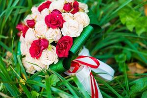 buquê de casamento de rosas vermelhas e brancas deitado na grama foto