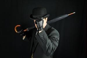 cavalheiro de terno escuro derrubando chapéu-coco em fundo preto. conceito de cavalheiro britânico clássico e excêntrico foto