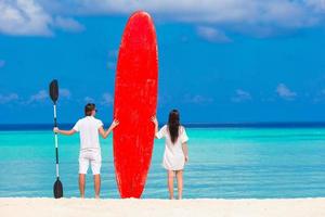 duas pessoas em pé na praia com uma prancha de paddle foto