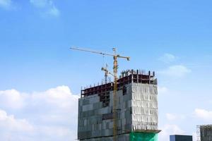 imagem remota de um edifício em construção com guindastes de elevação no céu azul brilhante e fundo nublado. foto