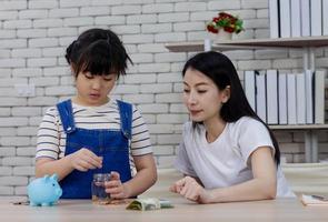 mãe ensina a filha a economizar dinheiro usando um cofrinho foto