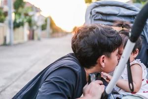 pai asiático e filha ou filho linda garota fazendo beijo sentindo-se feliz e desfrutando no carrinho de bebê pai e filho contato visual sorriso mostrando amor familiar à noite com luz solar no rosto felicidade foto