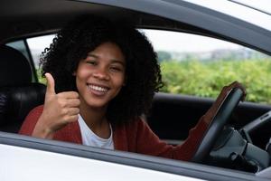 jovem meio asiático meio africano mostra o polegar para cima dentro do novo carro moderno. jovem emoção primeira viagem depois de passar no teste de carteira de motorista. se sente bem depois de comprar um carro novo. foto