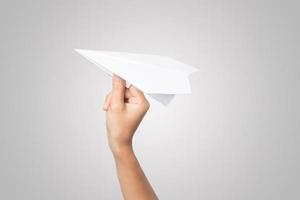 a mão de uma mulher segura um avião de papel no fundo branco foto