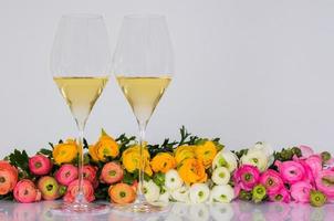 dois copos de vinho branco com flores coloridas de ranúnculo em fundo branco para o conceito de jantar dos namorados. foto