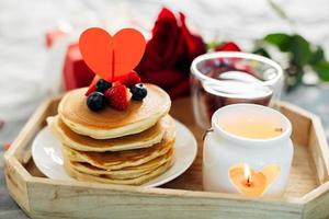 café da manhã ou brunch do dia dos namorados. panquecas caseiras com bagas, xícara de chá e rosas vermelhas. foto