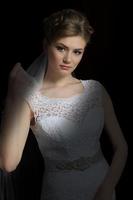 noiva linda com um penteado de casamento - em um fundo escuro. retrato de uma noiva linda. Casamento. a noiva de vestido branco segura um véu. foto