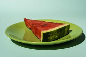 fatia de melancia em um prato em um fundo turquesa, vista lateral foto