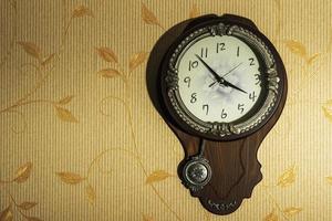 relógio de parede marrom redondo em casa com um pêndulo em uma parede clara foto