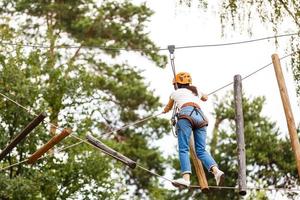 mulher com equipamento de escalada em um parque de aventura está envolvida em escalada ou passa por obstáculos na estrada de corda. foto