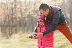 pai ensinando a filha a jogar tênis ao ar livre foto