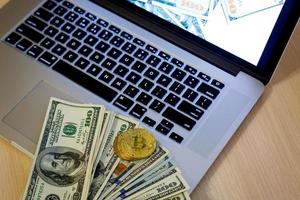 moedas de ouro bitcoin em um fundo de escritório de notas de dólar branco laptop móvel foto