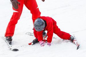 menina de vermelho aprendendo a esquiar com a ajuda de um adulto foto