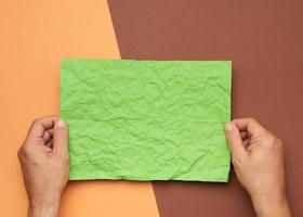 duas mãos masculinas estão segurando uma folha de papel verde amassada em branco sobre um fundo marrom foto