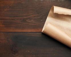 borda curvada de uma folha de papel pergaminho marrom em um fundo de madeira foto