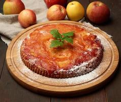 torta de maçã redonda assada na tábua de madeira e maçãs frescas foto