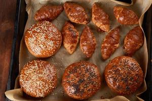 croissants assados e pães redondos com sementes de gergelim em uma assadeira de ferro com papel manteiga enrolado foto