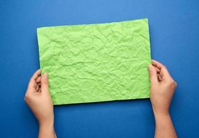 duas mãos femininas estão segurando uma folha de papel verde amassada em branco sobre fundo azul foto