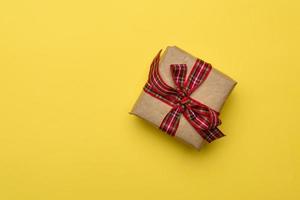 caixa quadrada com um presente embrulhado em papel pardo e amarrado com uma fita de seda vermelha foto