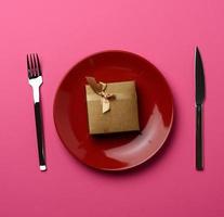 caixa de presente encontra-se em uma placa redonda de cerâmica e garfo com uma faca em um fundo rosa foto