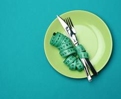 prato redondo verde e garfo e faca embrulhados em fita métrica verde sobre fundo azul foto