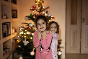 duas irmãs juntas perto da árvore de natal à noite em casa. foto