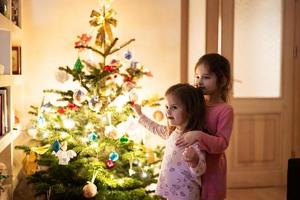 duas irmãs juntas perto da árvore de natal à noite em casa. foto
