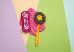 escovas de plástico rosa e pano para limpar a casa em um fundo colorido foto