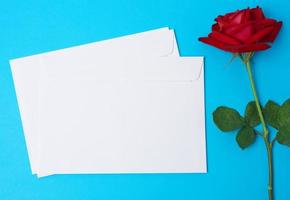 rosa vermelha florescendo e envelope de papel branco sobre um fundo azul foto