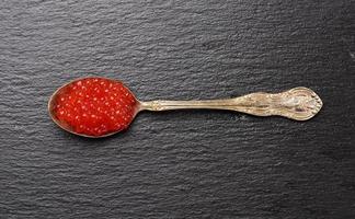 caviar vermelho de salmão amigo em uma colher de metal em um fundo preto foto