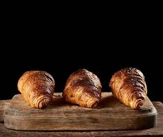 croissants assados na placa de cozinha marrom, fundo preto foto