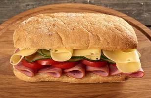 sanduíche com pão ciabatta, fatias finas de salsicha e queijo edam na tábua de madeira marrom foto