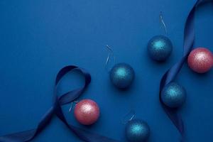 fita de seda e bolas de natal brilhantes rosa e azuis em um fundo azul foto