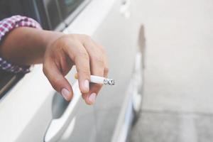 feche a mão do homem fumando um cigarro no carro durante a viagem de condução. estilo de vida saudável. ou não fumar conceito de campanha.