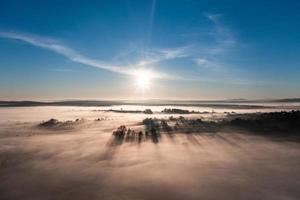 voando sobre uma aldeia ao amanhecer, sol brilhante no horizonte e neblina sobre uma pequena aldeia. foto