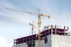 edifício em construção com guindastes trabalhando para mover materiais de construção sob o céu azul e a nuvem de seda. foto