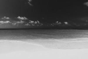 cena tranquila de praia em preto e branco. paisagem dramática da costa da ilha, céu escuro com águas calmas. costa tropical monocromática, areia fofa, beira-mar natural ao ar livre. férias de viagem de verão abstrato de luxo foto