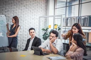 empresário cansado dormindo em uma conferência de reunião no escritório, pessoas da equipe de negócios olhando severamente para roncar na reunião foto