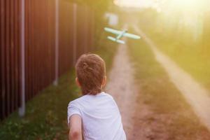 menino criança feliz brincando com avião de brinquedo ao ar livre ao pôr do sol foto