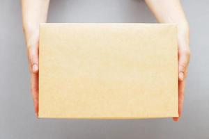mãos humanas segurando entrega caixa de papelão em fundo cinza. entrega e conceito de compras online. foto