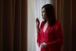 abra de uma mulher feliz em uma camisola vermelha, abrindo as cortinas da janela. foto