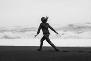 pessoa brincalhona correndo ao longo da fotografia cênica monocromática da praia do mar foto