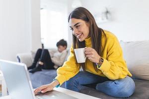 mãe sorridente trabalhando em casa com seu filho no sofá enquanto escreve um e-mail. jovem trabalhando em casa, enquanto estava em isolamento de quarentena durante a crise de saúde covid-19 foto