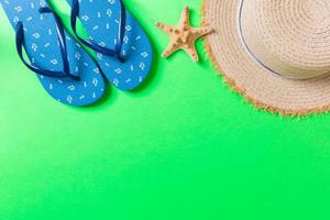 acessórios de configuração plana de praia de verão. chapéu de palha protetor solar, chinelos e conchas em fundo colorido. conceito de férias de viagem com espaço de cópia foto