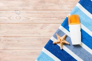 um frasco de protetor solar, toalha azul listrada e conchas em fundo de madeira. conceito de viagens de verão. vista superior com espaço de cópia foto