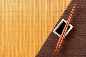 pauzinhos e tigela com molho de soja em duas esteira de bambu blak e vista superior amarela com espaço de cópia foto