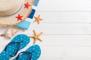 chapéu de palha, chinelos azuis, toalha e estrela do mar em um fundo branco de madeira. vista superior conceito de férias de verão com espaço de cópia foto