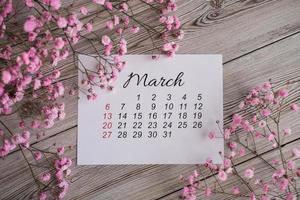 calendário de março de 2022 e flores cor de rosa em um fundo de madeira. calendário plano leigo foto