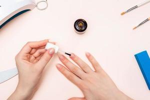 mãos de uma garota aplicando gel nas unhas com um pincel. A vista do topo foto